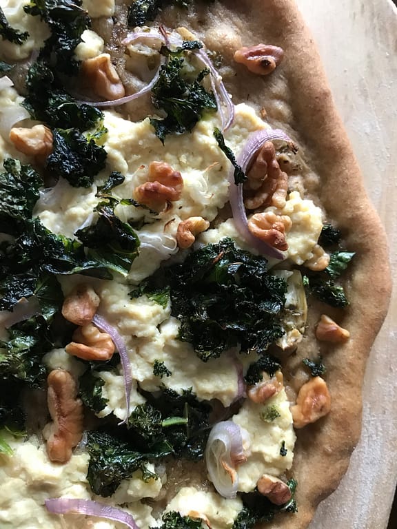 olive-oil-based pizza with vegan ricotta, kale, shallots, and walnuts