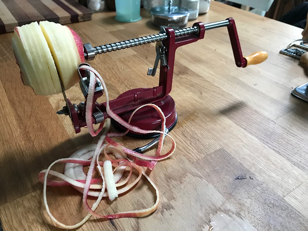 an apple on a red metal peeler-corer-slicer hand-crank tool