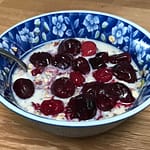 muesli in a blue bowl topped with cherries