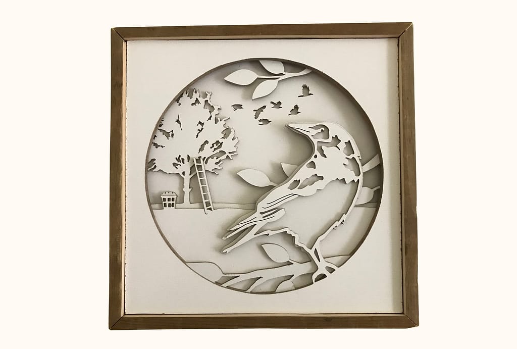 A crow shadowbox cut from layers of hardboard. In the foreground, a crow is perched in the branches. In the background, a flock of crows flies through the sky and a ladder leans up against an apple tree with a basket of apples at the bottom. 