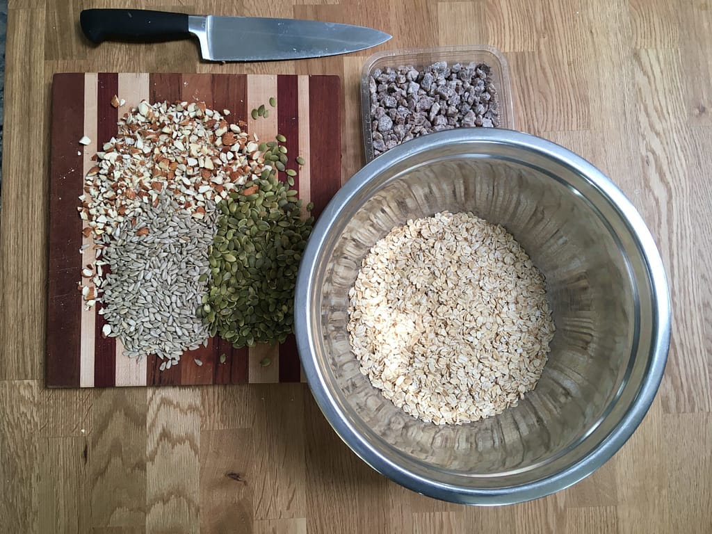 mixing bowl of muesli next to cutting board with chopped nuts