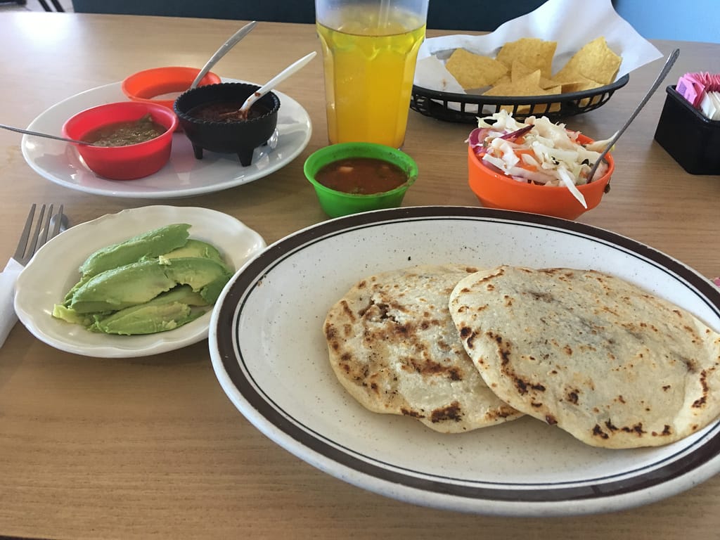 Freshly-made bean-filled pupusas, sliced avocados, 3 different moles, chips and salsa, cabbage slaw, and pineapple agua fresca. 