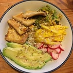 bowl full of sauteed tofu and cabbage, fresh mango and avocado, and pickled radish on top of rice