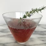 a cocktail glass of pomegranate spritzer with a rosemary sprig garnish