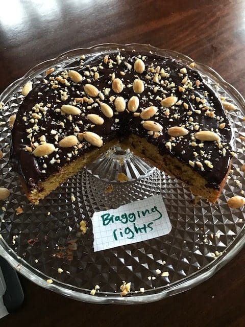 a cake with chocolate frosting topped with almonds. a large wedge is cut out of the cake, and in the empty space is a slip of paper that says "bragging rights."