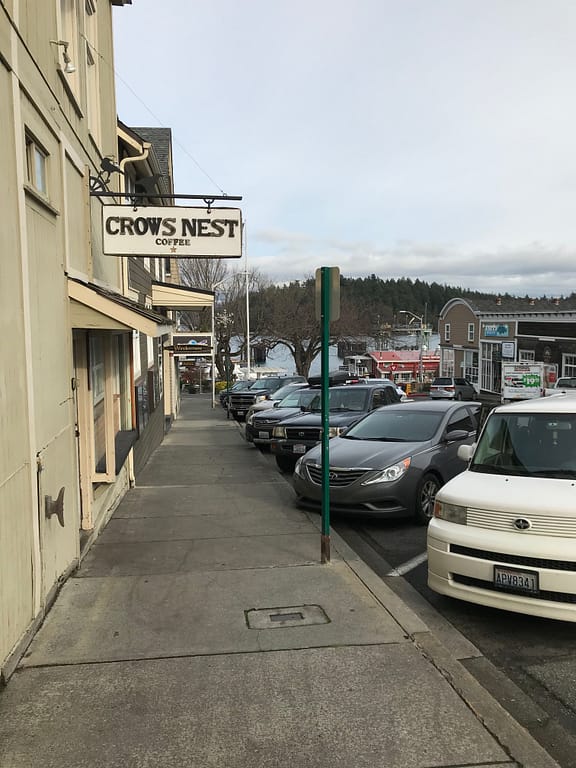 line of shops with the ferry dock in the distance. Sign reads, "Crows Nest coffee"