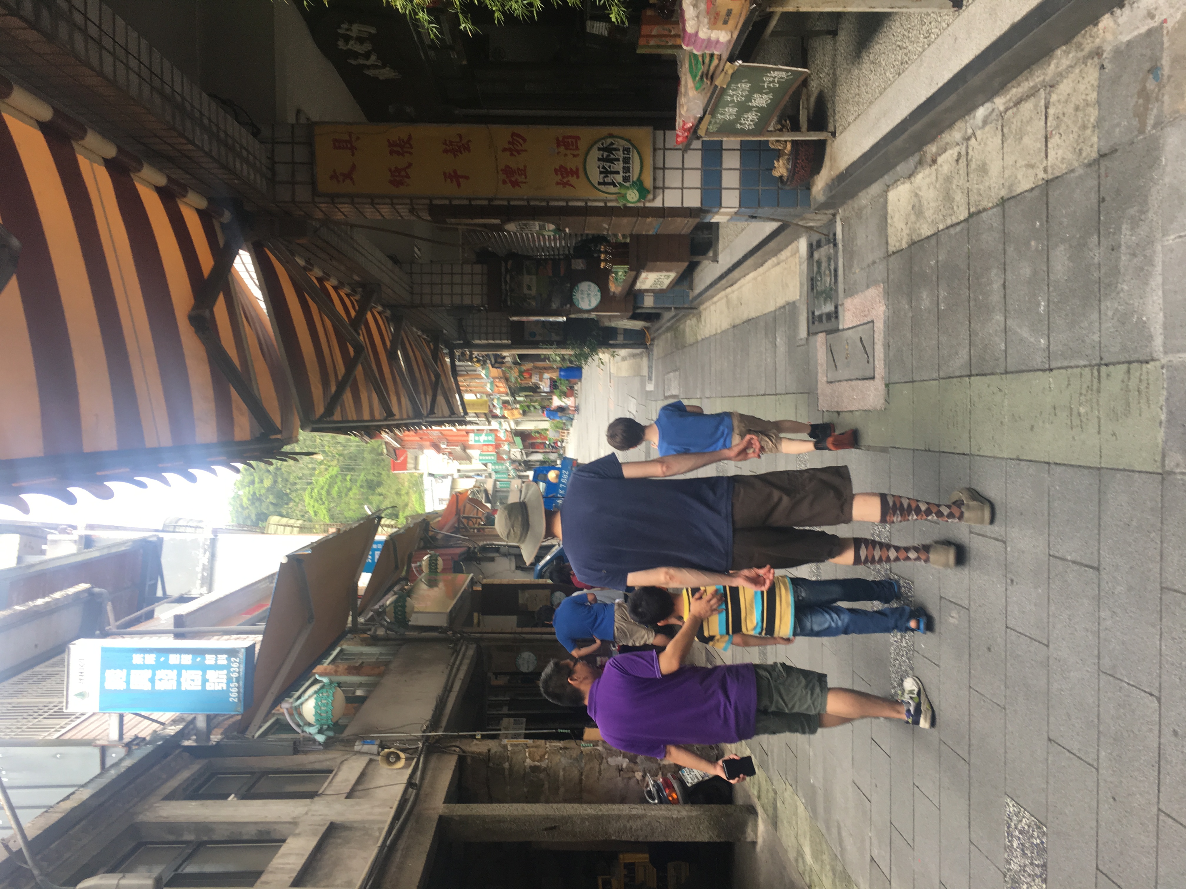 Four people walking through a narrow alleyway with small shops on either side.