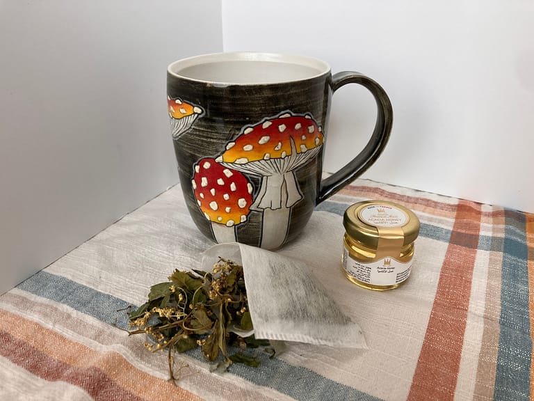 mushroom mug surrounded by a packet of herbal tea leaves and a small jar of honey